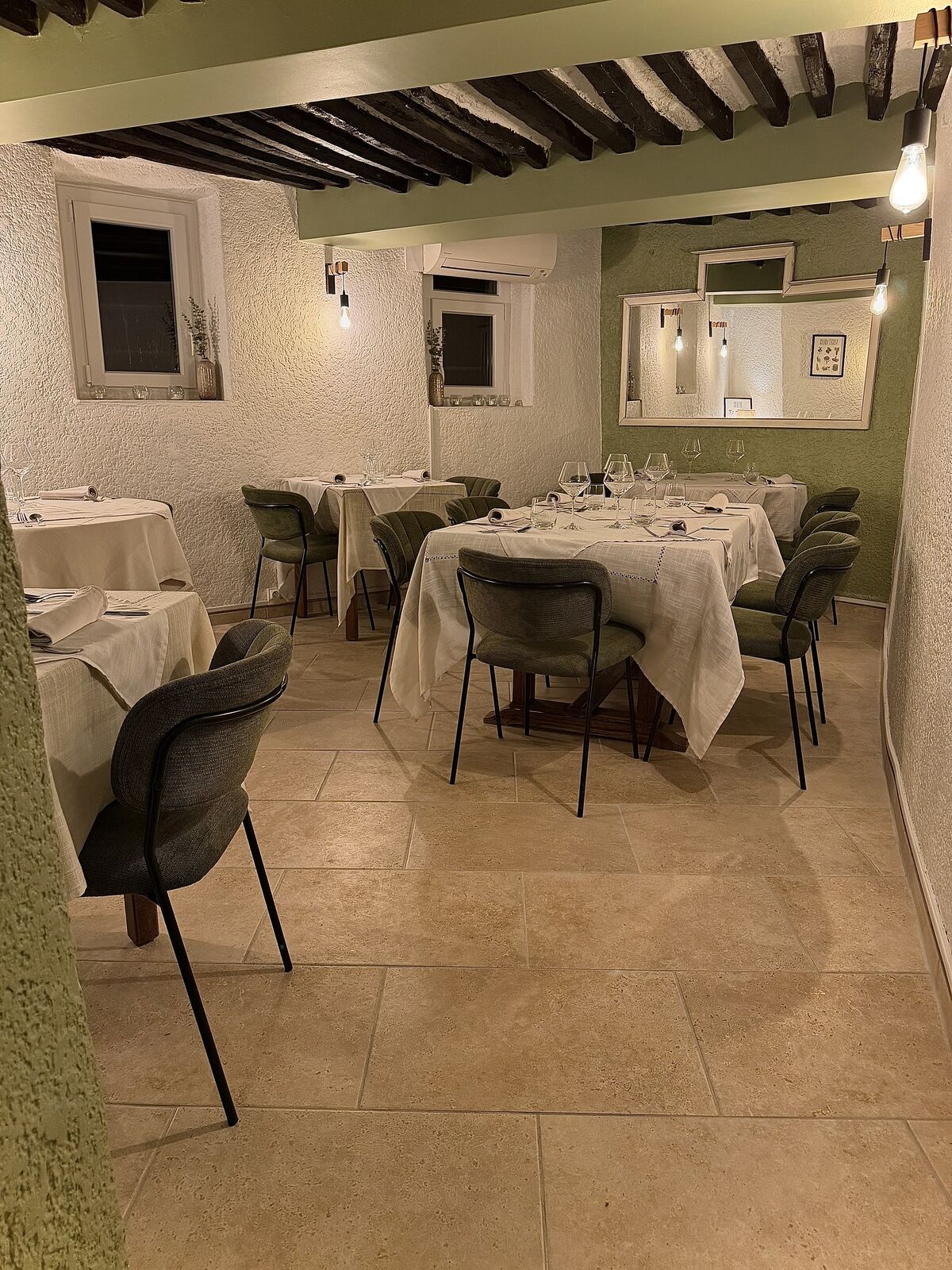 La salle du restaurant : murs vert sauge, poutres et tables nappées de blanc
